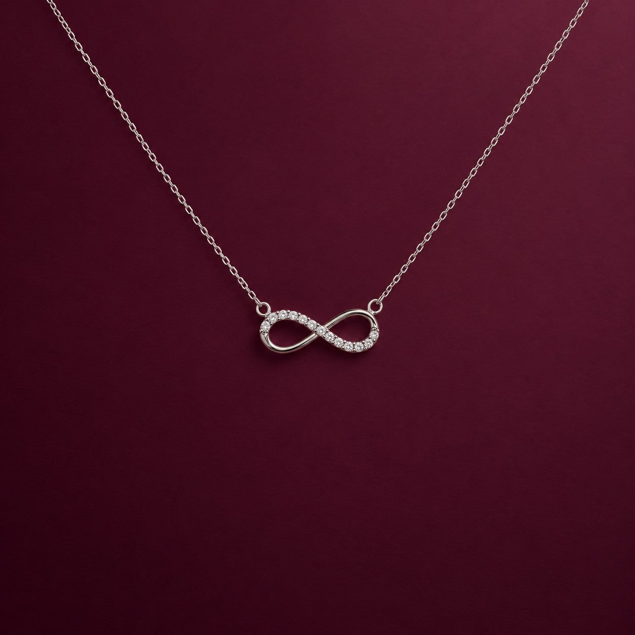 The Infinity silver pendant on a deep burgundy background, Silvk 925 silver jewellery