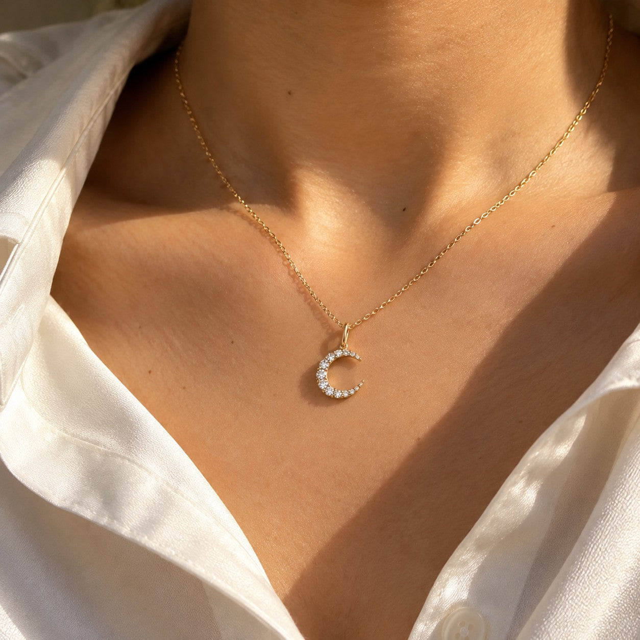 The Moon gold crescent pendant worn on the neck with a cream top, Silvk 925 silver jewellery