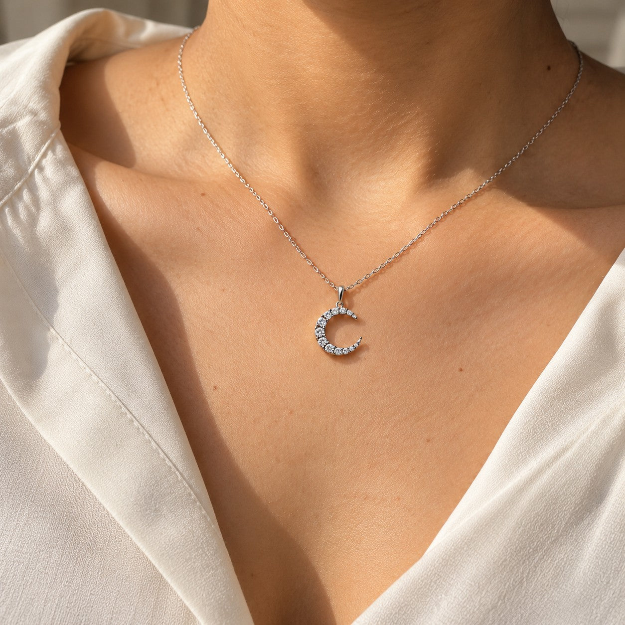 The Moon silver crescent pendant worn on the neck with a cream top, Silvk 925 silver jewellery